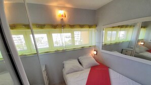 Une chambre à coucher avec un lit, une table de chevet, un miroir et une fenêtre avec des rideaux.