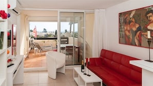 Een moderne woonkamer met een rode bank, een witte salontafel en een glazen schuindeur die uitkomt op een balkon met zitplaatsen.