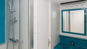 Een badkamer met een glazen douchecabine, een witte deur, een blauwe wastafel en een spiegel met een blauwe lijst.