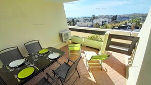 Varanda com mesa de jantar posta para quatro, espaço de estar ao ar livre e vista para a cidade.