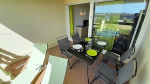 Varanda com mesa posta para refeições, cadeiras e vista para o exterior.