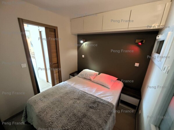 A bedroom with a bed, bedside tables, a wardrobe, and a door leading to a balcony. - Apartment "PROHIBITION" (LE CAP D AGDE)