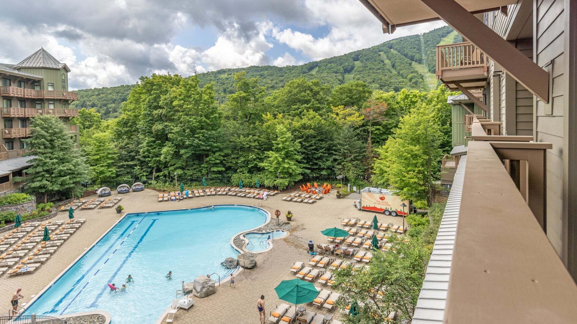 Ein Hotelpoolbereich mit großem Pool, Liegestühlen und Blick auf einen bewaldeten Berg.