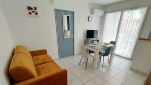 A living room with a sofa, a dining table with chairs, a TV, and a door. - Bright one-bedroom apartment, air conditioning and parking - 4VOIL245 (CANET PLAGE)