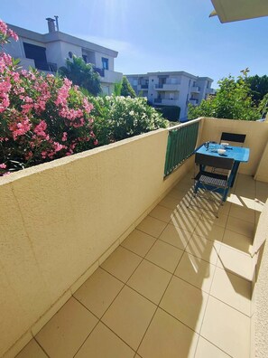 A balcony with a tiled floor, a table with chairs, and a view of neighboring buildings.