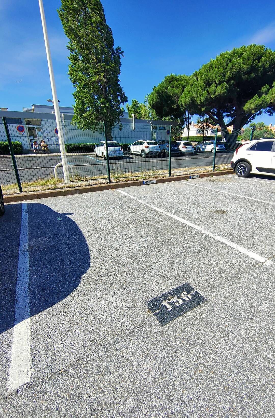 Een parkeerplaats met aanduidingen, een hek en een gebouw op de achtergrond.