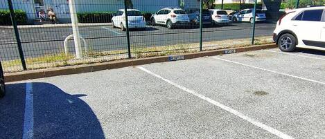 Een parkeerplaats met aanduidingen, een hek en een gebouw op de achtergrond.