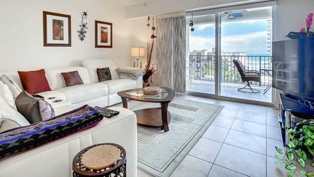 Un salon moderne avec un canapé blanc, une table basse, un ventilateur de plafond et un balcon offrant une vue dégagée.