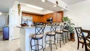 Une cuisine moderne avec des meubles en bois, un îlot central doté de tabourets de bar et un réfrigérateur.