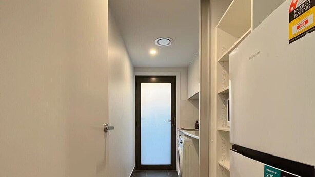 A narrow hallway with a washing machine, a refrigerator, and a door leading to another room.