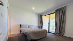 A bedroom with a bed, a radiator, a window with curtains, and a door.
