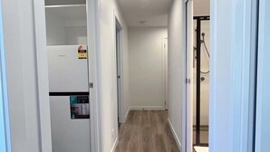 A hallway with wooden flooring, white walls, and a refrigerator with a sticker.