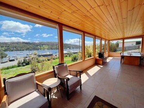 A covered patio with large windows, a wooden ceiling, and a view of a lake and boats. - Coastal Cabin next to Bruny Island Ferry (Kettering)