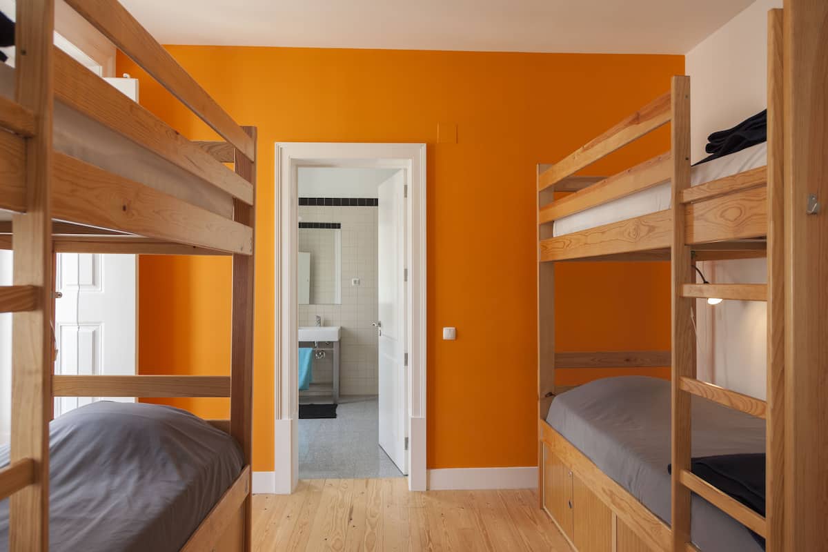 A room with bunk beds, an open door leading to a bathroom, and wooden flooring.