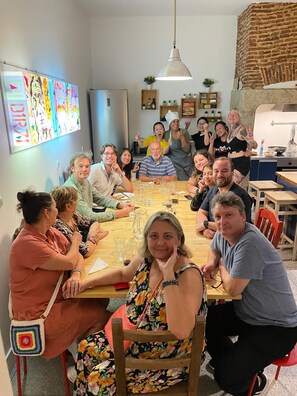 Un grupo de personas sentadas alrededor de una mesa de madera en una habitación con pared de ladrillo, una lámpara colgante y un televisor de pared que muestra gráficos coloridos.