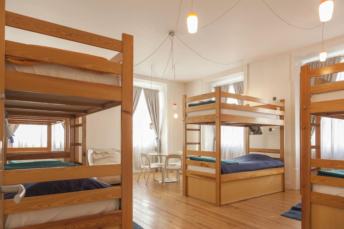 A room with bunk beds, a small table, chairs, and a window with curtains.