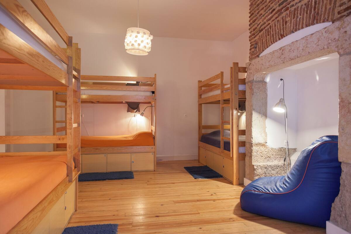 A bunk bed room with a blue bean bag chair, wooden floors, and a hanging light fixture.