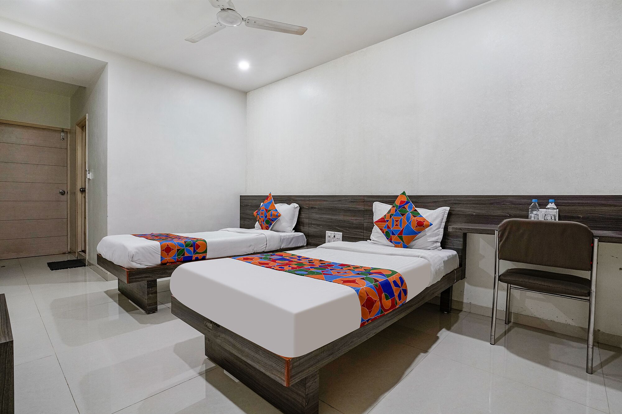A hotel room with two beds, a wooden headboard, a ceiling fan, and a chair.