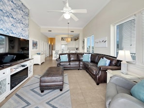 A spacious living room with a leather sectional sofa, a TV, and a ceiling fan. - Wave n' Sea:  3 bed 3 bath (Navarre Beach)