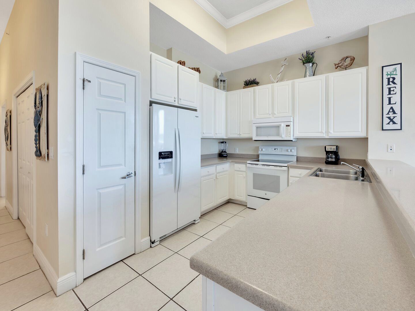 A modern kitchen with white cabinetry, a built-in oven, microwave, and refrigerator. There is a countertop with a sink and a coffee maker.