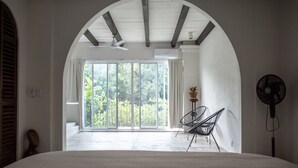 Een slaapkamer met een groot bed, een plafondventilator, een stoel en uitzicht op de omgeving door een glazen deur.