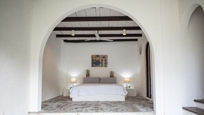 Een slaapkamer met een bed centraal onder een gewelfde plafond, met aan weerszijden twee nachtkastjes met lampen.