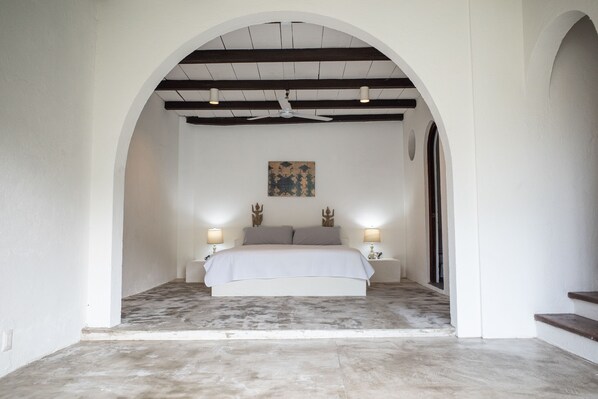 A bedroom with a bed centered under an arched ceiling, flanked by two bedside tables with lamps.