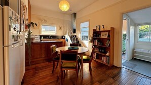 A kitchen with wooden flooring, a dining table with chairs, a refrigerator, and a bookshelf.