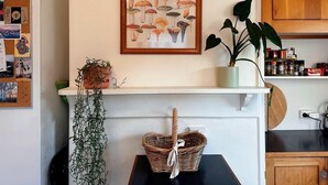 A kitchen with a corkboard, a framed mushroom poster, a potted plant, a wicker basket, and a wooden cabinet.