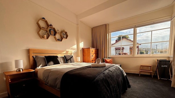 A hotel room with a bed, bedside tables, a window with a view, and a dark-colored carpet.