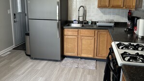 A modern kitchen with wooden cabinets, a stainless steel refrigerator, a gas stove, and a tiled backsplash. - Lake/Beach Getaway (Remodeled) (Round Lake Beach)