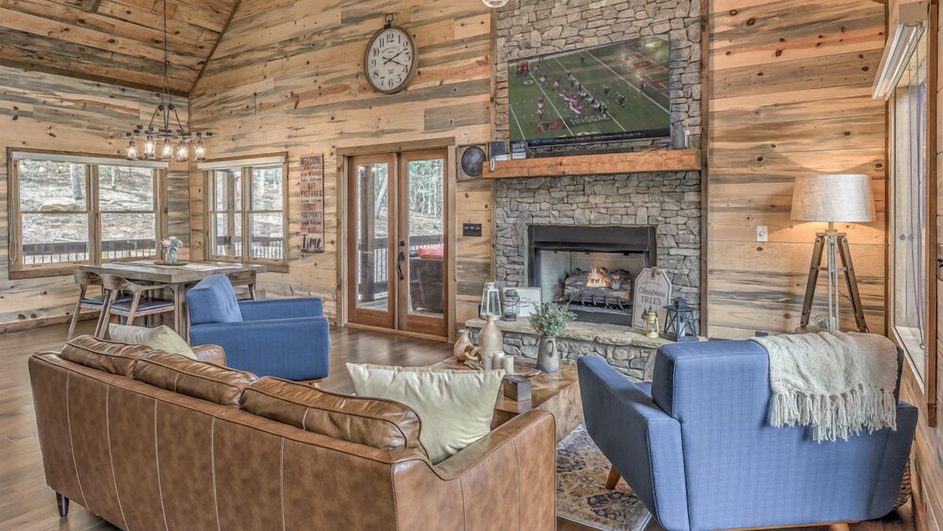 A cozy cabin interior with a stone fireplace, wooden walls, and a television mounted above it.