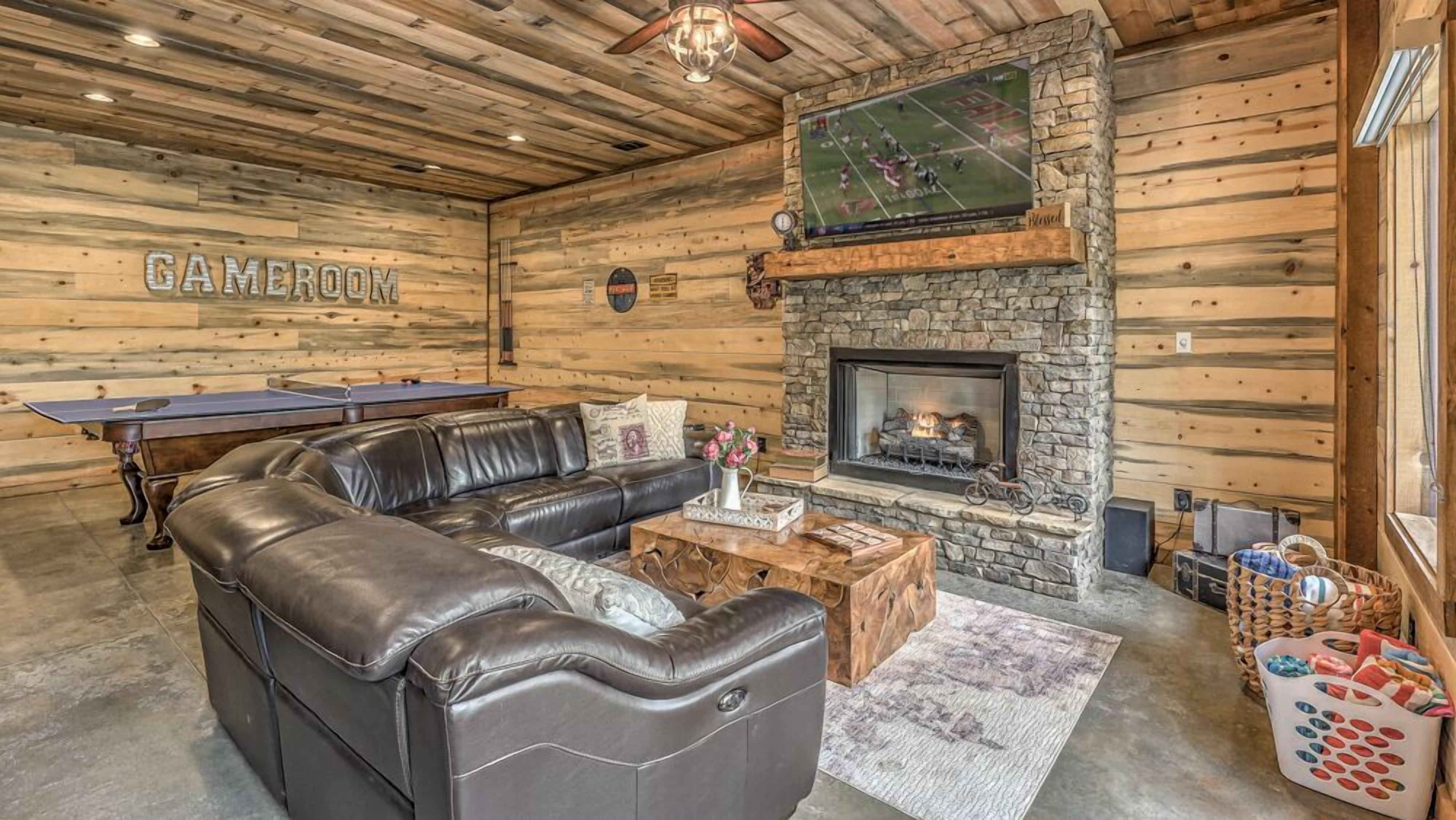 A cozy room with a leather sofa, a pool table, and a stone fireplace.