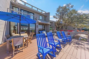A wooden deck with outdoor furniture, including chairs and a table, under a blue umbrella. - Luxurious Harbour Town Villa with a stunning patio space overlooking the water and golf course! (Hilton Head Island)