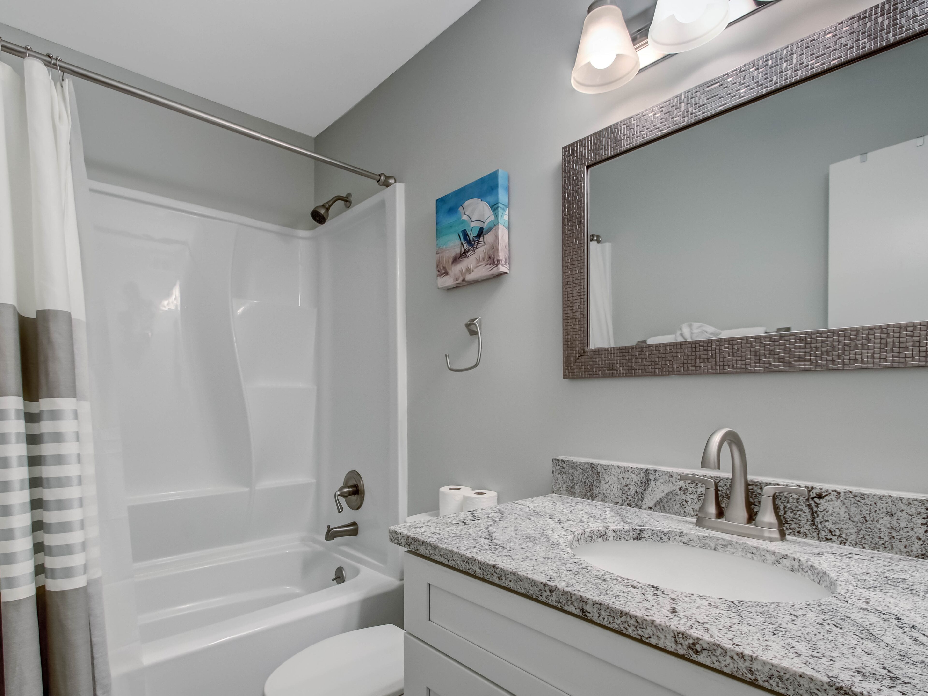 A bathroom with a bathtub, a sink with a marble countertop, a mirror with a textured frame, and a shower curtain.