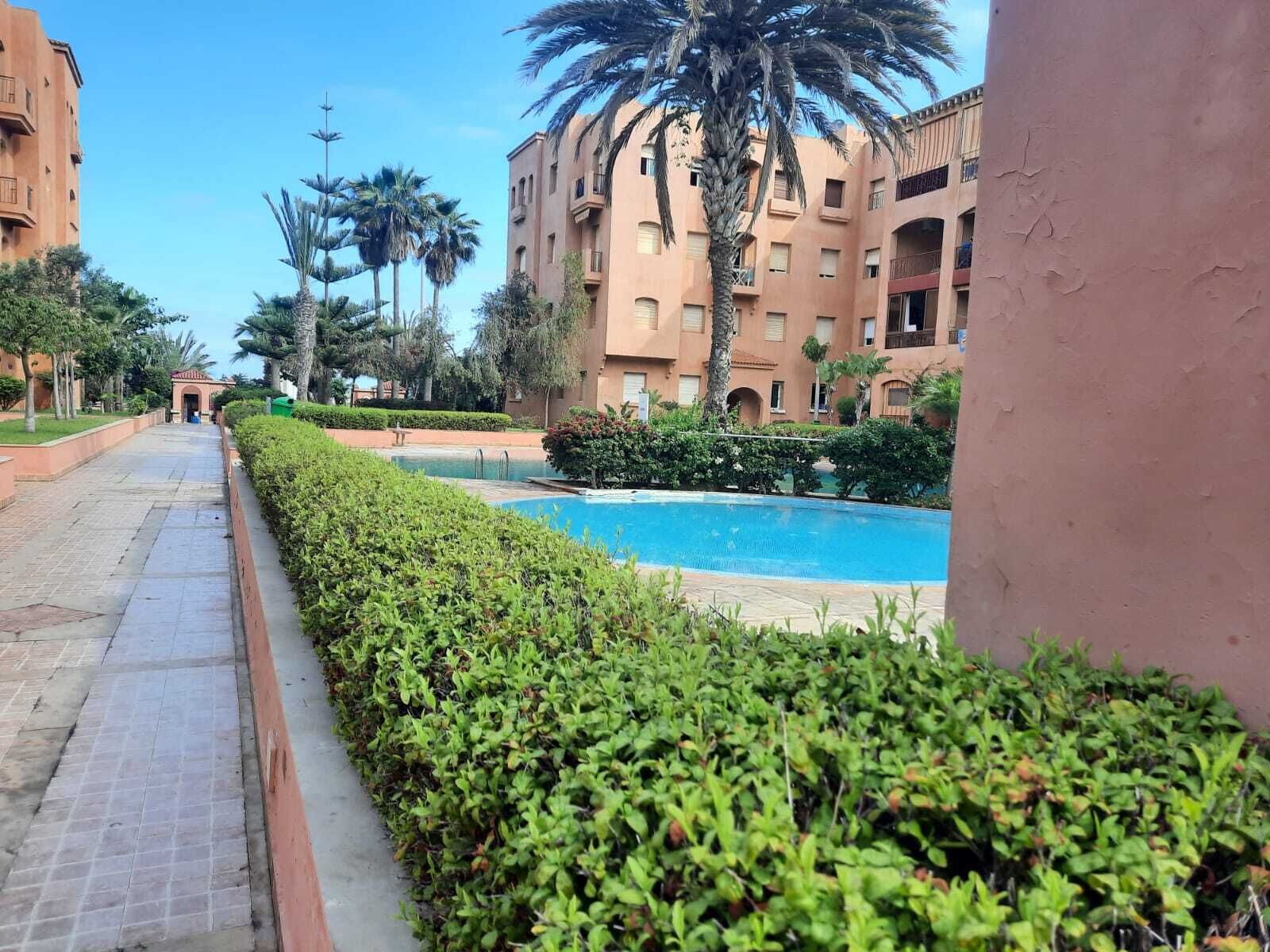 A pool area with a clear pathway, surrounded by well-maintained hedges and palm trees.