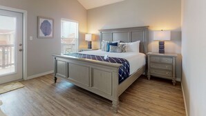 A bedroom with a large bed, two bedside tables, a ceiling fan, and a door with a view. - Walk to the Beach, Shared Heated Pool, Golf Cart Access (Port Aransas)