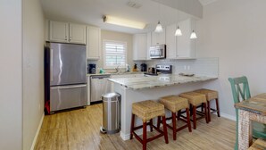 A modern kitchen with stainless steel appliances, a central island with bar stools, and a wooden floor. - Walk to the Beach, Shared Heated Pool, Golf Cart Access (Port Aransas)