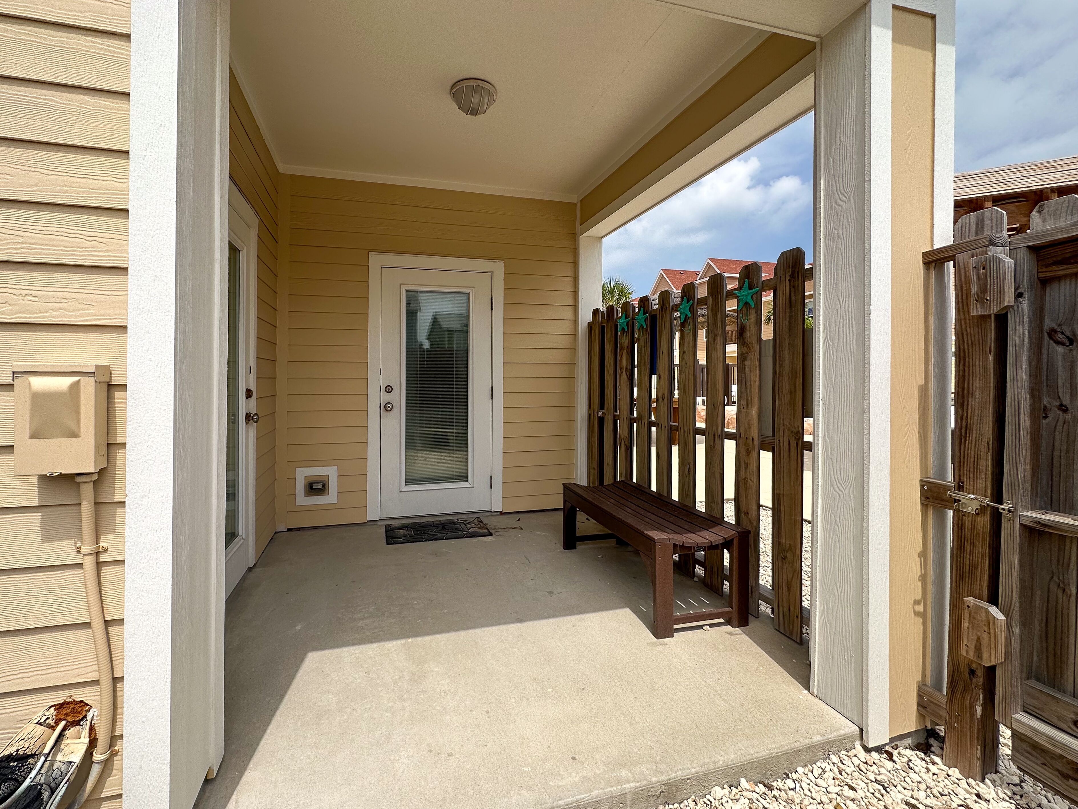 A covered porch with a bench, a door, and a wooden fence.