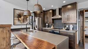 Une cuisine moderne dotée d’un grand îlot central, d’appareils électroménagers en acier inoxydable et de meubles de rangement en bois.