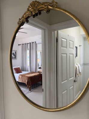 A bedroom with a bed, a door, and a mirror reflecting the room.