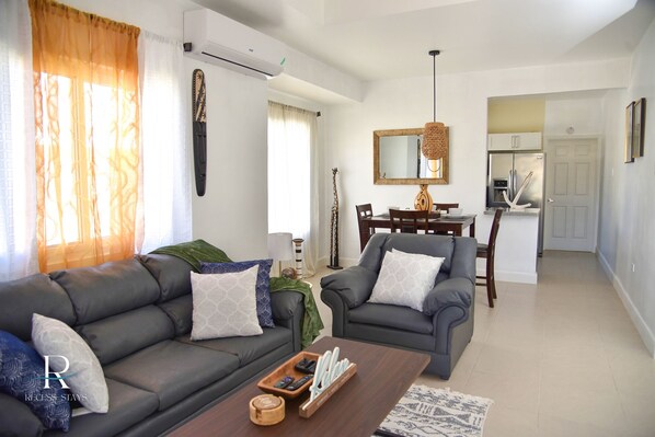 A modern living room with two grey sofas, a coffee table, and a dining area with a chandelier.