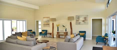 A spacious living room with two grey sofas, a coffee table, and a ceiling fan. There are two lamps on the wall, a painting, and a small wooden table.