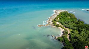 An aerial view of a coastal area with a clear path along the beach, surrounded by lush greenery and calm waters.