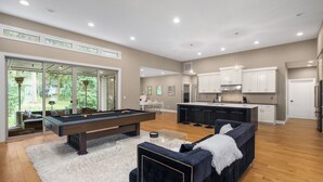 A spacious living area with a pool table, a dark blue sofa, and a kitchen in the background. - Large Open Home - Gourmet Kitchen - Pool Table (Portland)