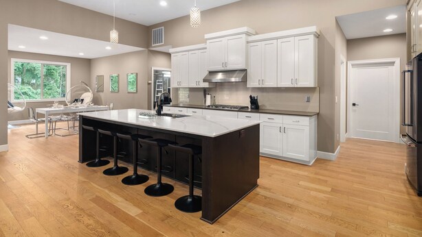 A modern kitchen with a large island, white cabinets, and a wooden floor. - Large Open Home - Gourmet Kitchen - Pool Table (Portland)