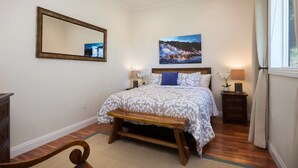 Ein Schlafzimmer mit Bett, Nachttisch, Lampe, Spiegel und einem Bild an der Wand.