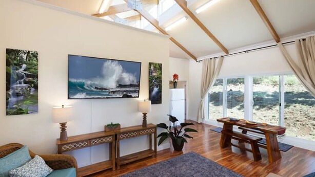 Ein geräumiger Wohnbereich mit einer hölzernen Bank, einer Couch und einem großen Fenster mit Blick auf den Strand.
