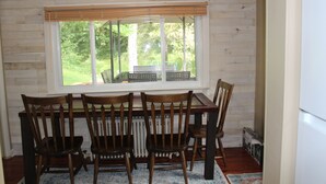 Un comedor con mesa y sillas de madera, una ventana con vistas a zonas verdes, y un radiador debajo de la ventana.
