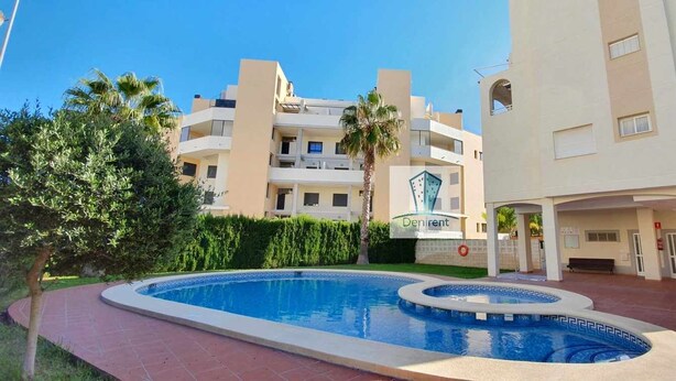 A modern building with a swimming pool, palm trees, and a sign reading "Denirent." - Apartment 150 meters from the beach, 500 meters from Denia (Denia)